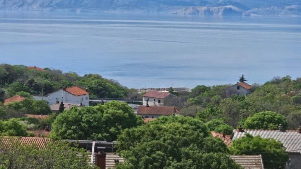 View of the roofs of red and white houses with green trees in the foreground and a view of the sea in the background, ideal for real estate in Croatia