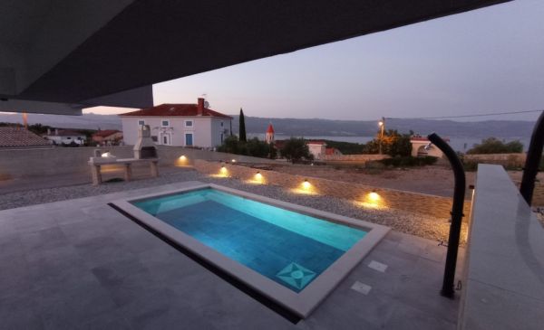 Evening view of a property in Croatia with an illuminated pool and a view of the sea in the background.