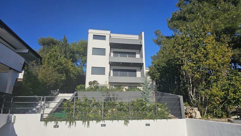 Exterior view of a contemporary apartment building for sale in Crikvenica surrounded by lush greenery with sea views