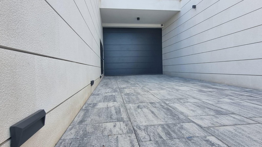 Driveway and garage of a modern residential building in Croatia with paved floor and gray gate.