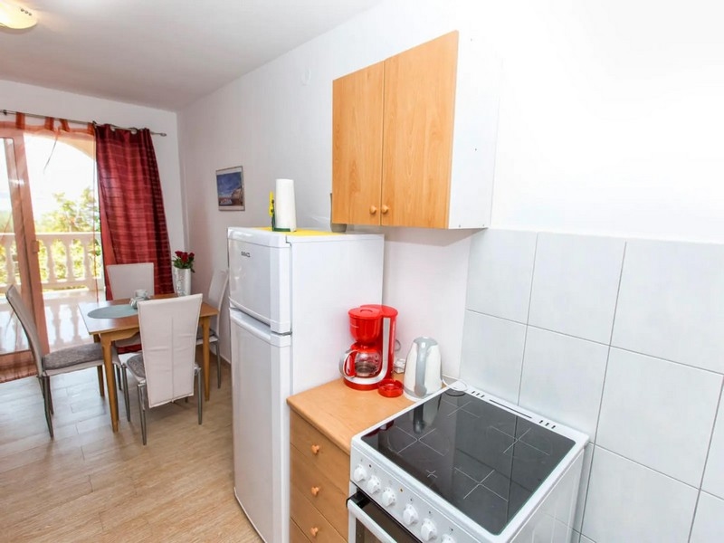 Compact kitchen with white appliances, wooden cabinets and a small dining area leading out to a balcony.