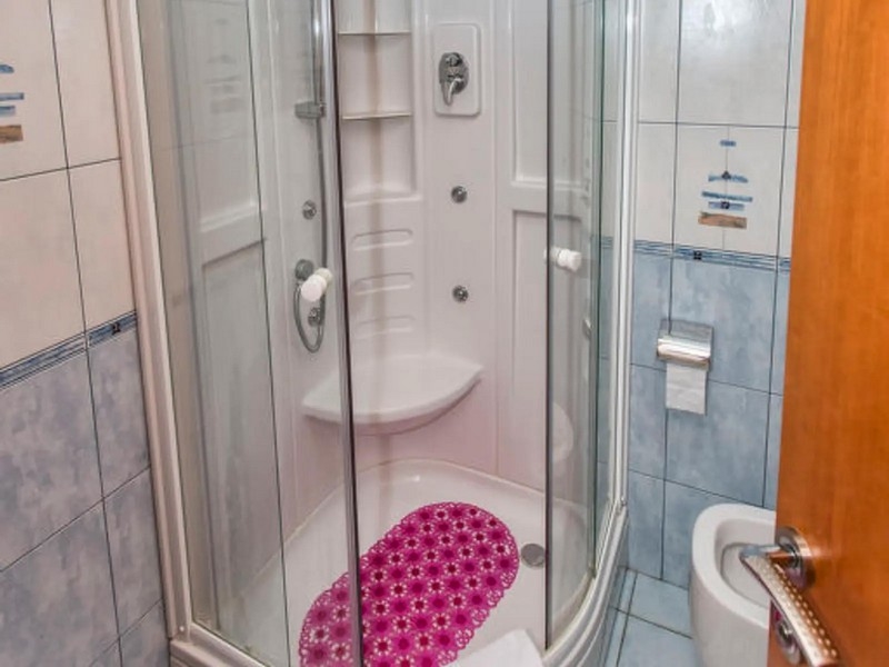 Bathroom with corner shower cubicle, blue and white tiles and various bathroom accessories, suitable for seaside properties in Croatia.