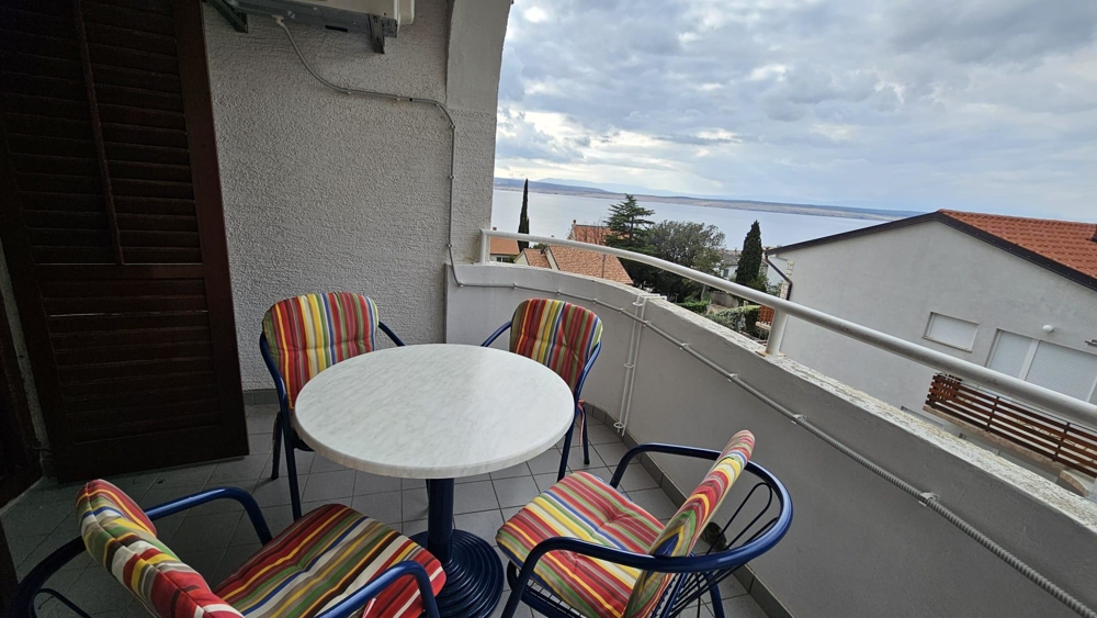 Balcony interior with round table and four colorful striped chairs overlooking the sea.