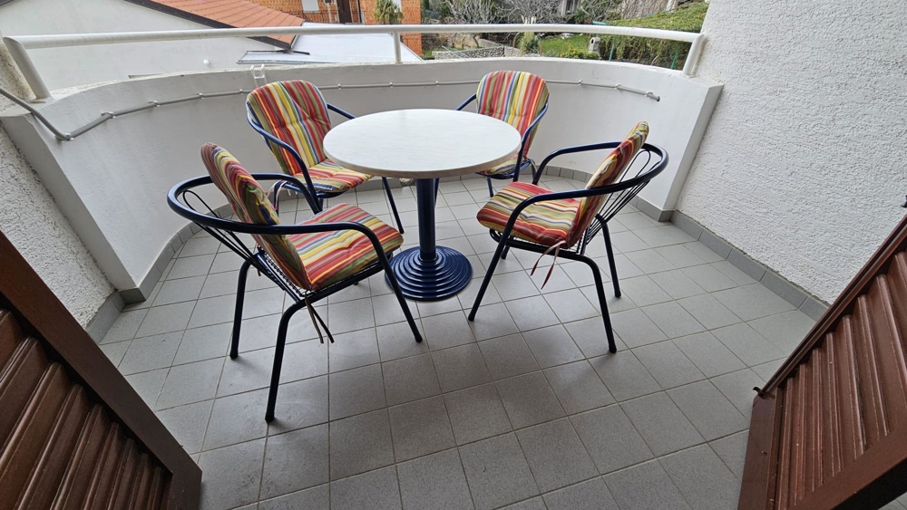 Close-up of balcony area with table and chairs, tiled floor and partial view of neighboring building.