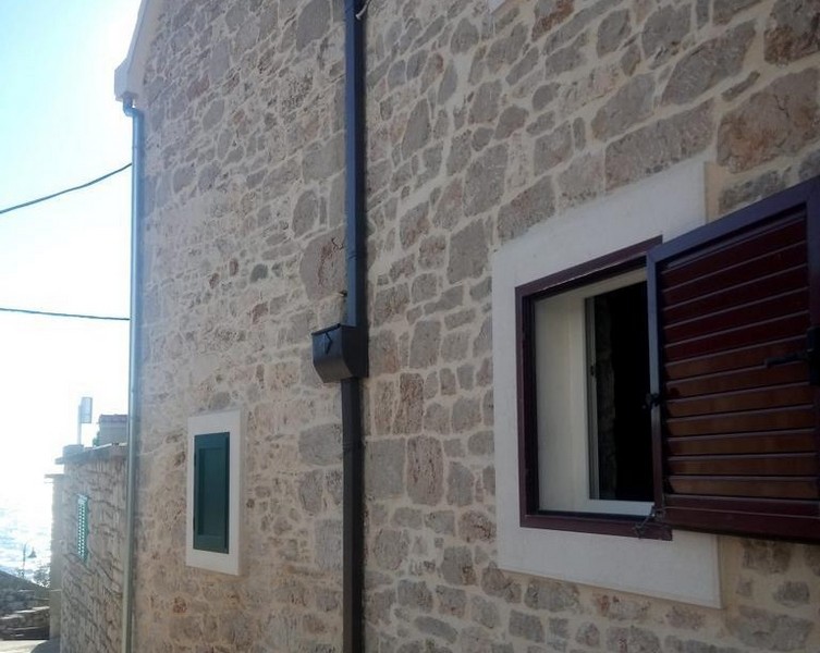 Side view of the stone house in Primošten with exposed bricks and windows with wooden shutters