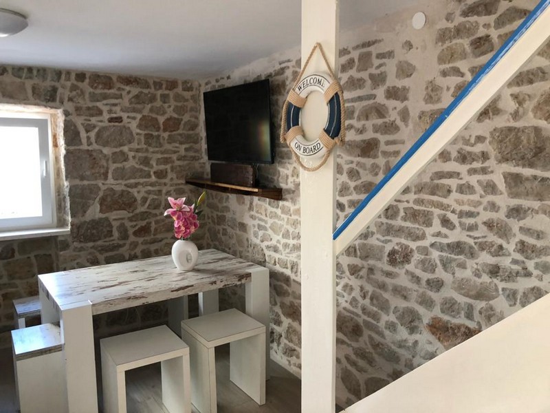 Interior view of the stone house with stone walls, TV and a small dining table, maritime decor