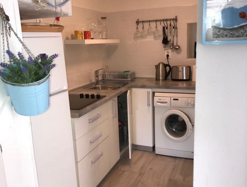 Compact kitchen in stone house with modern white cabinets, stainless steel sink and built-in washing machine