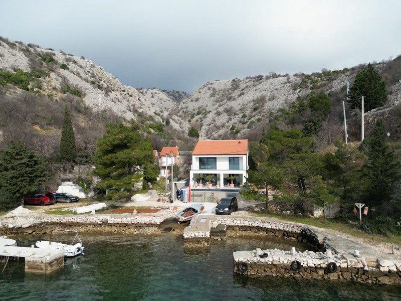Aerial view of seafront villa with boat dock and parked cars in Croatia