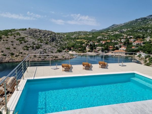 Exterior view of a seafront apartment building for sale in Karlobag, Croatia, with an infinity pool and coastal views